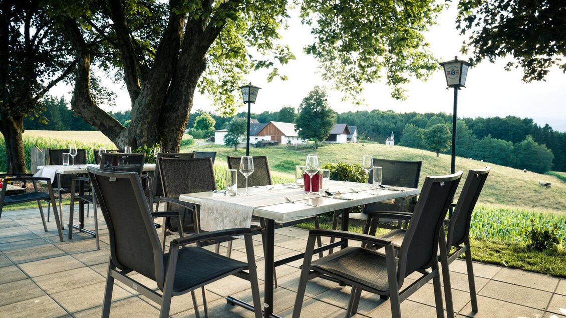 Eine gemütliche Terrasse mit eleganten Tischen und Stühlen. Im Hintergrund sind grüne Felder und einige Häuser zu sehen. | © Martinhof