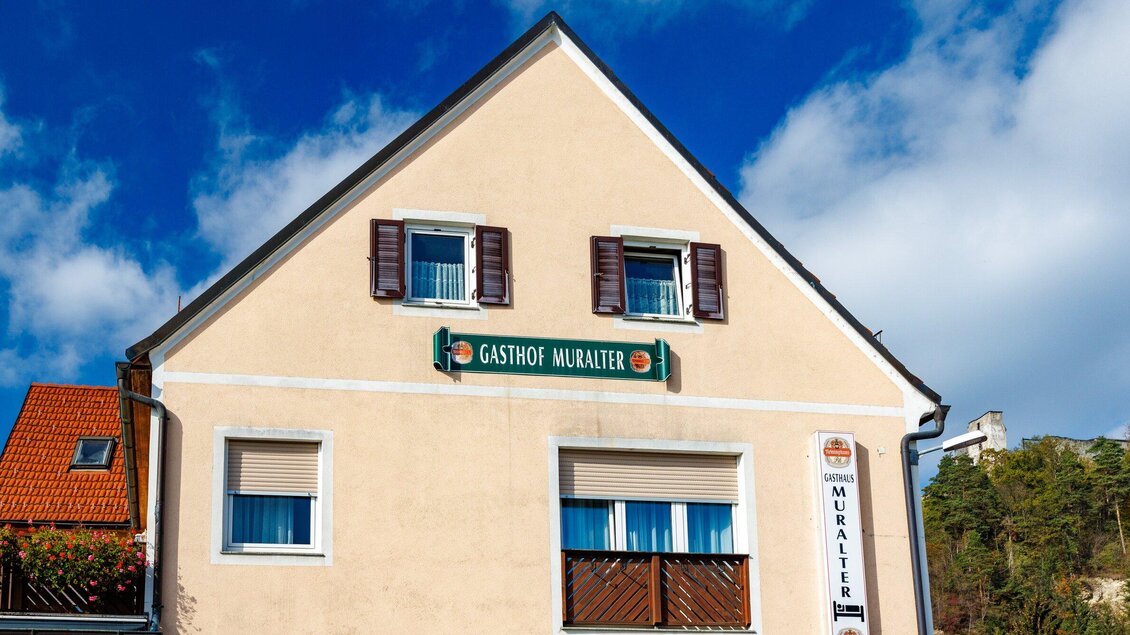 Ein traditionelles Gasthaus mit der Aufschrift "Gasthof Muralter". Die Fassade ist hell und freundlich, umgeben von einem blauen Himmel. | © TV Region Graz-Harry Schiffer