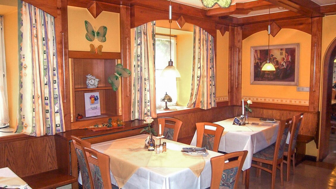 Ein gemütliches Restaurant mit Holzelementen und eleganter Tischdekoration. Die Wände sind mit bunten Vorhängen und Bildern geschmückt. | © Gasthof Niggas "Kranerwirt"