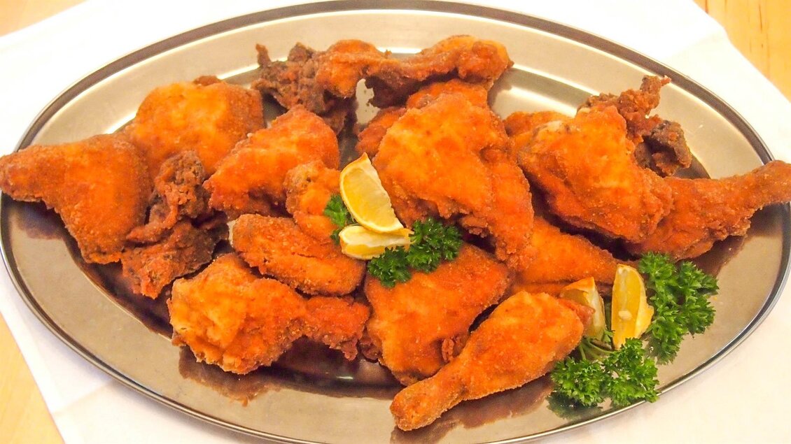 Ein Teller mit knusprigem frittiertem Hühnchen, garniert mit Zitronenscheiben und Petersilie. Die goldene Farbgebung macht das Gericht besonders appetitlich. | © Gasthof Niggas "Kranerwirt"