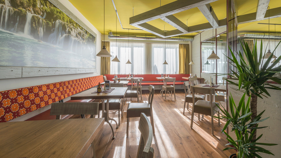Ein modernes Restaurant mit Holztischen und gemütlicher Einrichtung. Große Fenster lassen viel Tageslicht herein und es gibt Pflanzen zur Dekoration. | © TV Hochsteiermark
