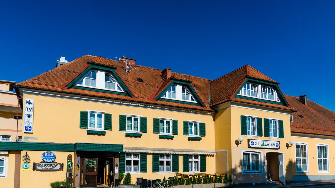 Ein charmantes gelbes Gebäude mit roten Dächern und grünen Fensterläden. Die Fassade wirkt einladend und hat ein traditionelles Design. | © TV Region Graz - MiasPhotoart