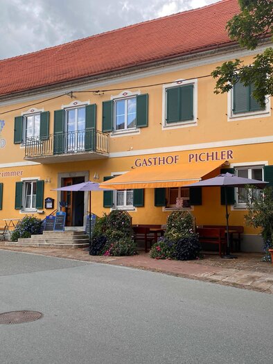 Ein gelbes Gasthaus mit dem Namen "Gasthof Pichler". Vor dem Gebäude stehen Tische und Stühle unter Sonnenschirmen. | © Gasthof Pichler