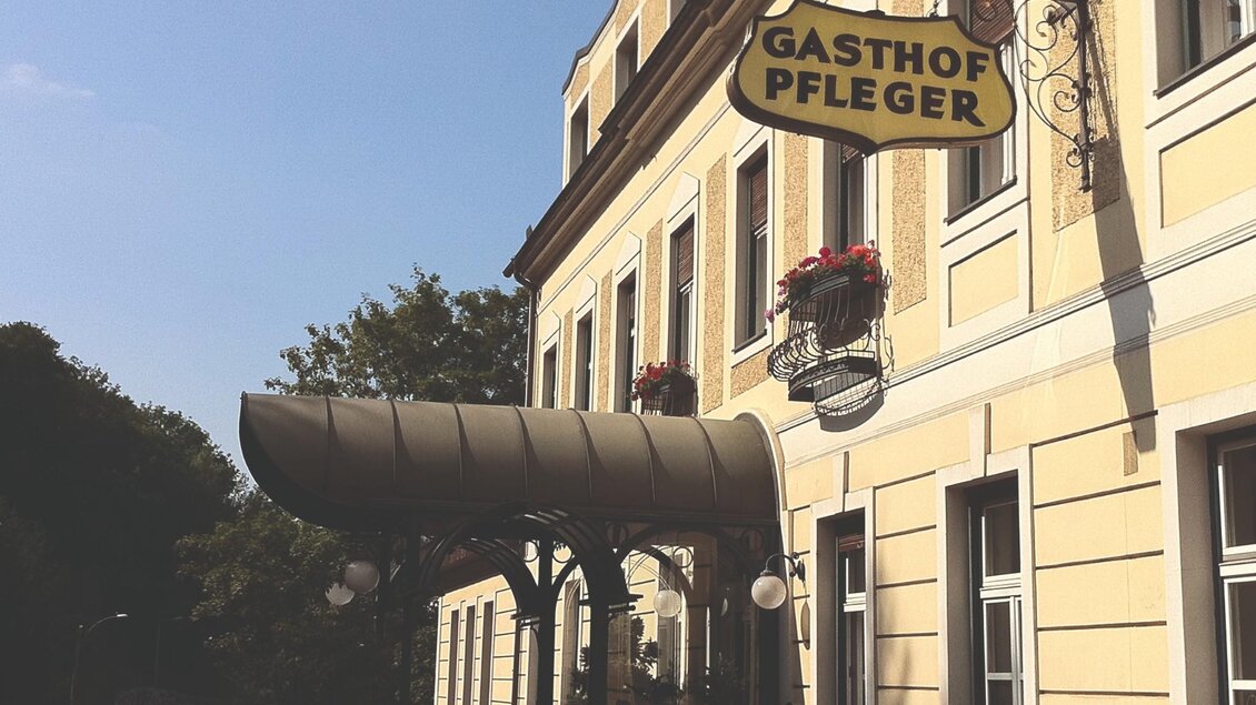 Ein rustikales Schild mit der Aufschrift „Gasthof Pfleger“. Das Schild hängt an der Fassade eines Gebäudes. | © Gasthof Pfleger