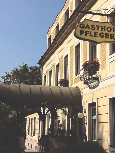A rustic sign with the inscription "Gasthof Pfleger". The sign hangs on the facade of a building. | © Gasthof Pfleger
