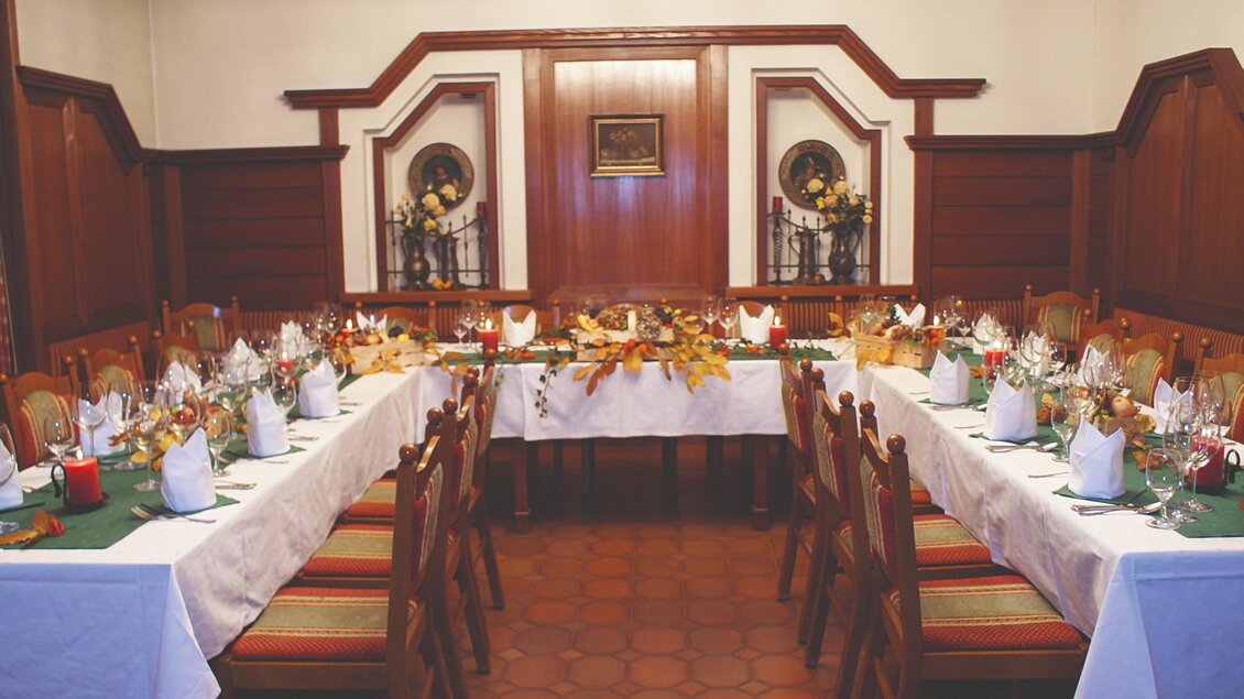 Ein festlich gedeckter Tisch mit weißer Tischdecke, grünen Stoffservietten und Kerzen. Der Raum ist in warmen Holztönen gehalten, und die Dekoration enthält herbstliche Elemente wie Blätter und Früchte. | © Gasthof Pfleger