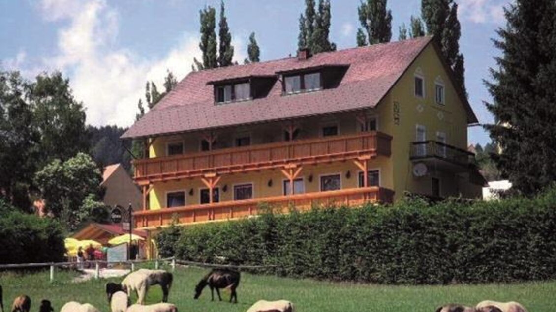 Ein buntes Haus umgeben von Bäumen und Wiesen. Auf der Wiese grasen mehrere Pferde. | © Günter Bardel