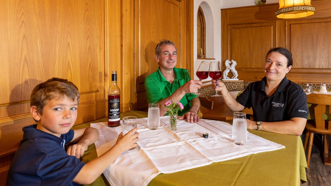 Eine fröhliche Familie sitzt an einem Tisch in einem gemütlichen Restaurant. Sie stoßen mit Getränken an und genießen ihre Zeit zusammen. | © Lipizzanerheimat | Harry Schiffer