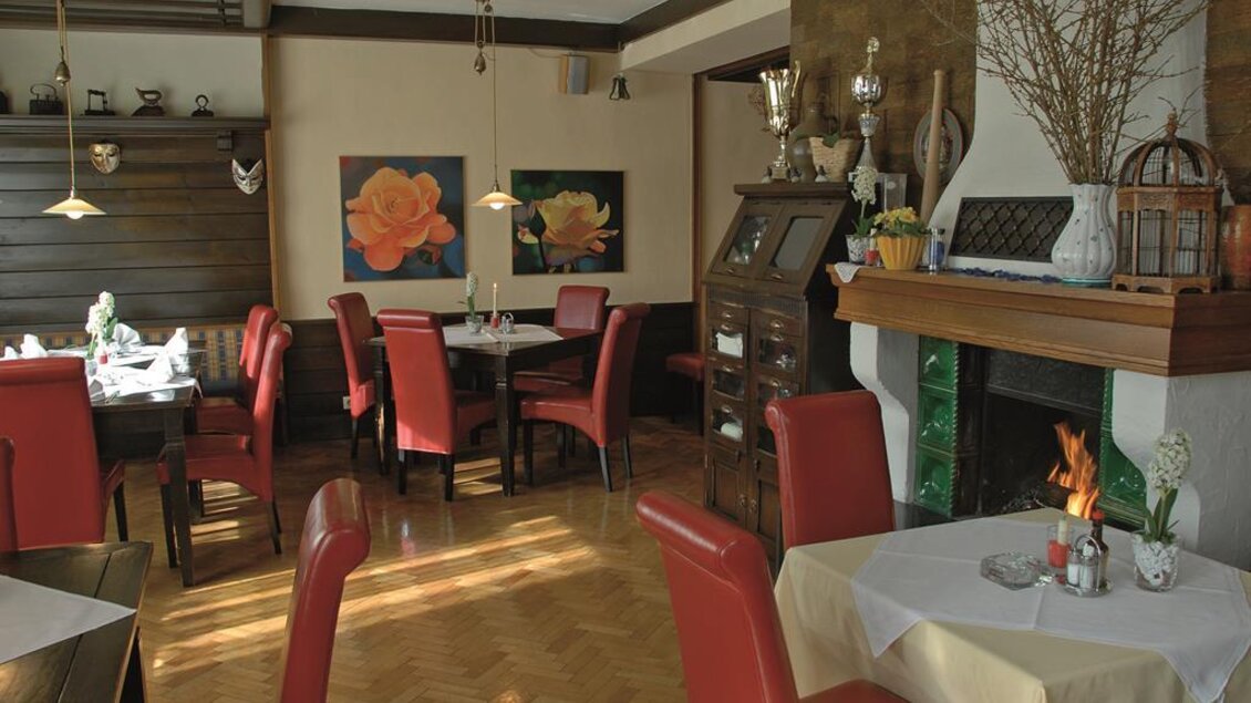 Ein einladendes Restaurant mit roten Stühlen und einem Kamin. An den Wänden hängen Blumenbilder, die eine gemütliche Atmosphäre schaffen. | © Familie Reinisch