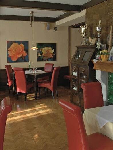 Ein einladendes Restaurant mit roten Stühlen und einem Kamin. An den Wänden hängen Blumenbilder, die eine gemütliche Atmosphäre schaffen. | © Familie Reinisch