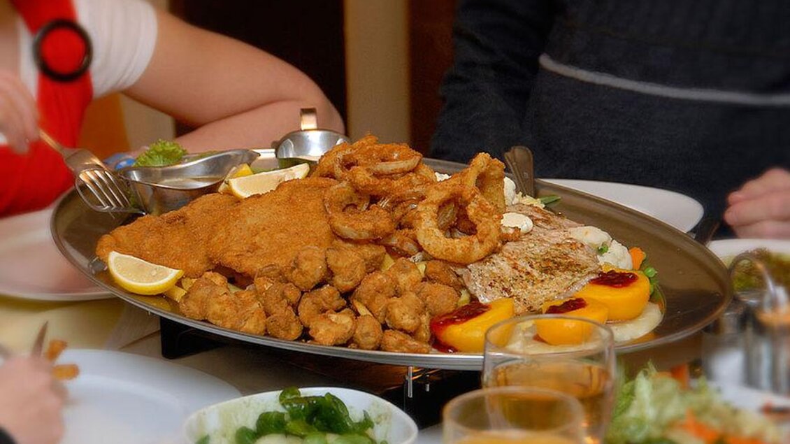 Ein großes Essen auf einer silbernen Platte, das verschiedene frittierte Speisen wie Hähnchen und Tintenfisch enthält. Rundherum sind verschiedene Beilagen und Getränke zu sehen. | © Familie Reinisch