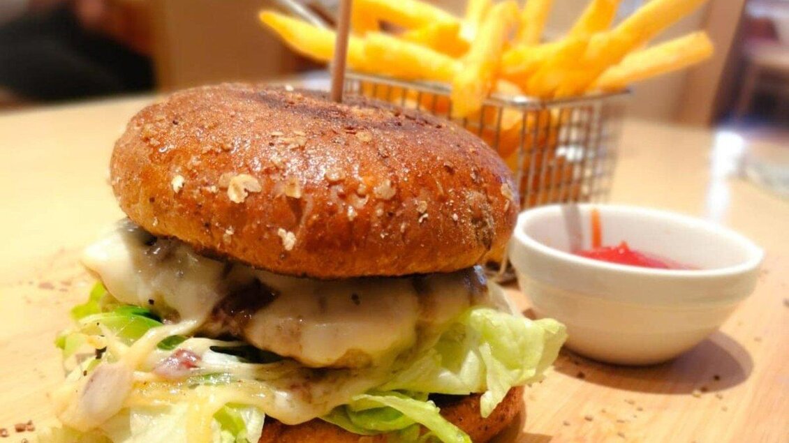 Ein saftiger Burger mit Schmelzkäse, Salat und einem ganzen Brötchen. Dazu gibt es knusprige Pommes Frites und eine kleine Schüssel Ketchup. | © Fam. Reinisch