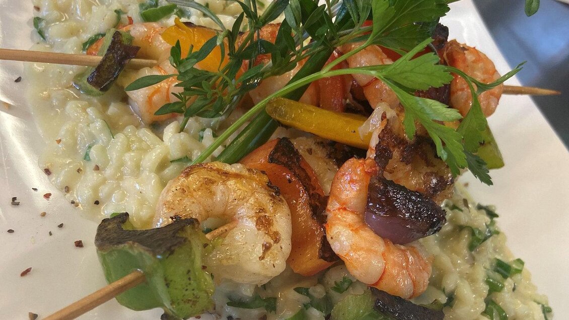 Ein köstliches Gericht mit frischen Garnelen und Gemüse-Spießen auf einem Bett aus cremigem Risotto. Das Gericht ist mit Kräutern garniert und ansprechend angerichtet. | © Fam. Reinisch