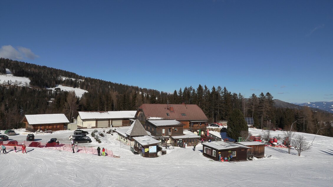 Ein gemütliches Hüttenrestaurant in den Bergen, umgeben von schneebedeckten Landschaften. Der Himmel ist klar und blau, mit einigen Bäumen im Hintergrund. | © Gasthof Rieseralm