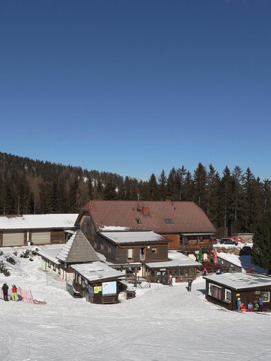 A cozy hut restaurant in the mountains, surrounded by snow-covered landscapes. The sky is clear and blue, with some trees in the background. | © Gasthof Rieseralm
