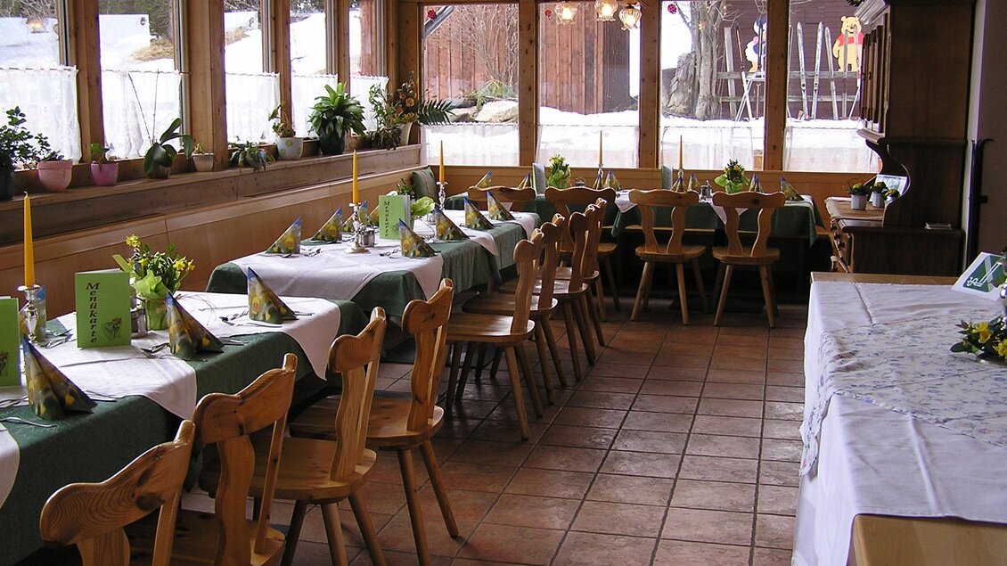 Ein gemütlicher Restaurantbereich mit Holztischen und Stühlen. Die Tische sind aufwendig gedeckt und der Raum hat große Fenster mit Blick auf die Außenlandschaft. | © Gasthof Rieseralm