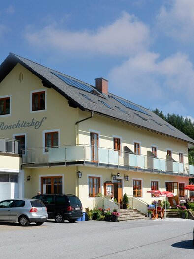 Ein gemütliches Gasthaus mit einem hellen Außenbereich und Sonnenschirmen. Umgeben von Bäumen und einer ruhigen Landschaft. | © Gasthof Roschitzhof