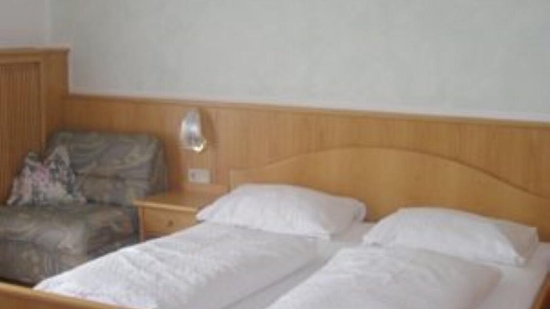 Ein einfaches Schlafzimmer mit einem Doppelbett und einem Sofa. Die Wände sind hellgrün, und es gibt ein dekoratives Bild an der Wand. | © Gasthof Roschitzhof