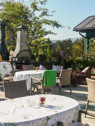 A beautiful outdoor area of a restaurant with covered tables and chairs. The surroundings are green and sunny, ideal for a relaxed meal outside. | © GH Safran Filatsch
