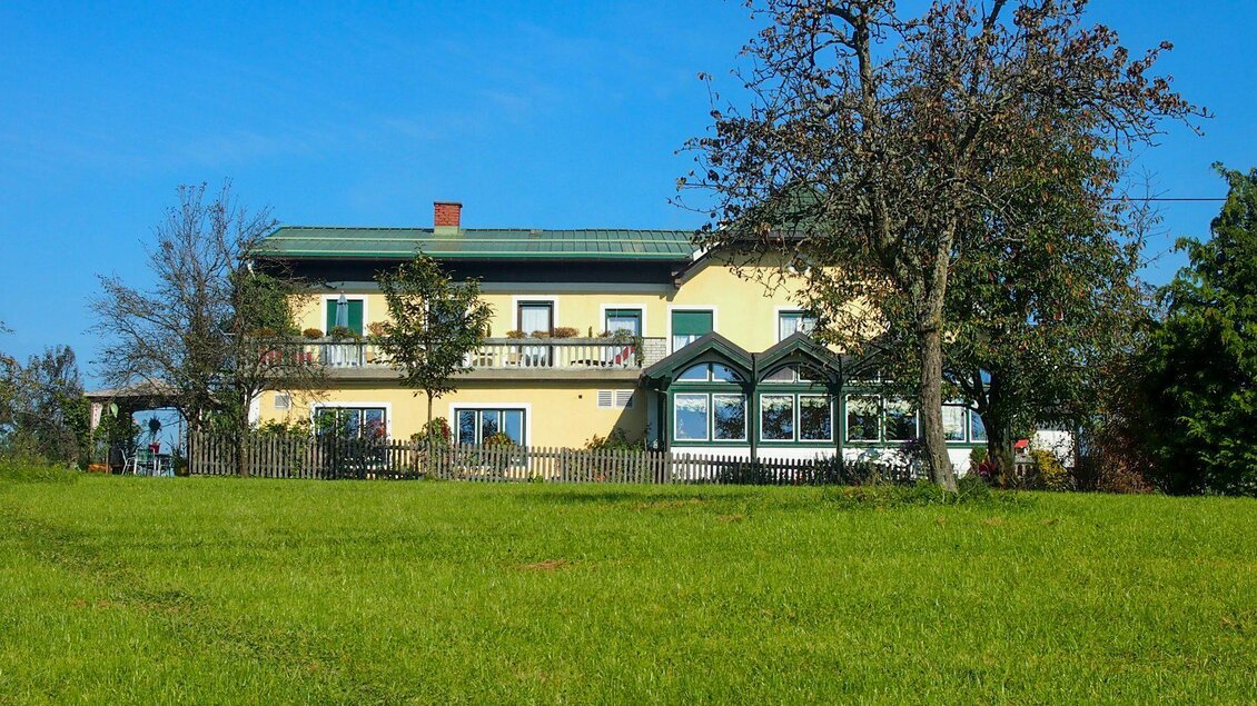 Ein gelbes Haus mit grünen Fensterläden steht auf einer Wiese. Der Himmel ist blau und es gibt einige Bäume in der Umgebung. | © GH Safran Filatsch