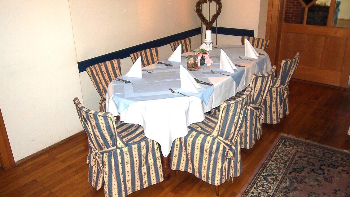 Ein dekorierter Tisch mit weißen Tischdecken und gefalteten Servietten steht in einem gemütlichen Raum. Rund um den Tisch sind gepolsterte Stühle mit gestreifter Bezug. | © GH Safran Filatsch