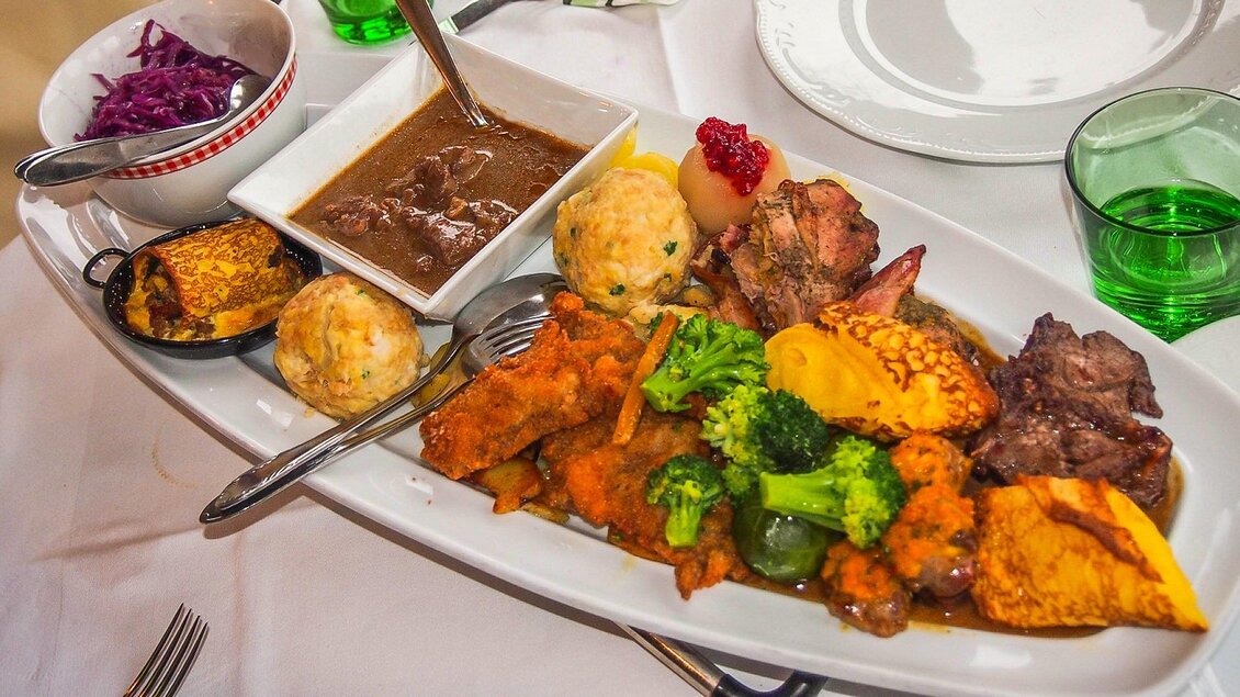 Ein reichhaltiger Teller mit verschiedenen Fleischgerichten, Gemüse und Beilagen. Dazu gibt es Soße und Salat in kleinen Schalen. | © GH Safran Filatsch