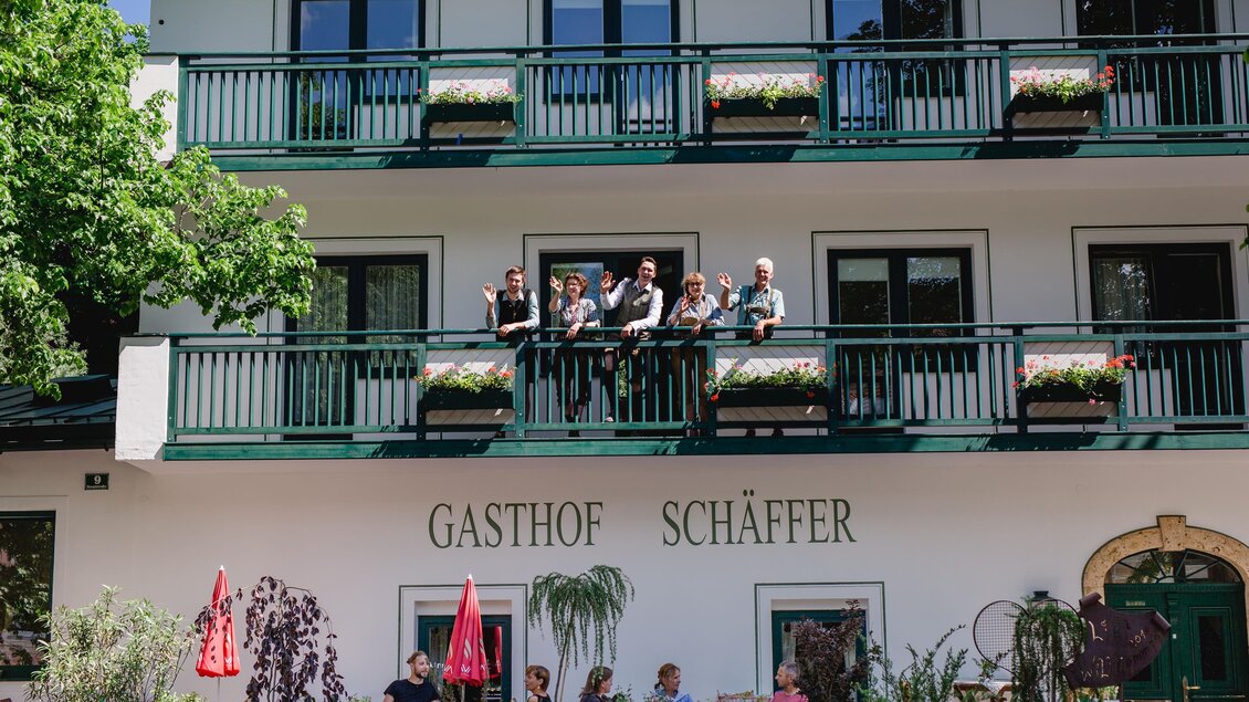 Ein Gasthof mit dem Namen „Schäffer“ und einer Terrasse im Vordergrund. Auf dem Balkon stehen mehrere Personen, umgeben von Pflanzen und Blumen. | © GH Schäffer_Neuberg (C) Seiser_Karner
