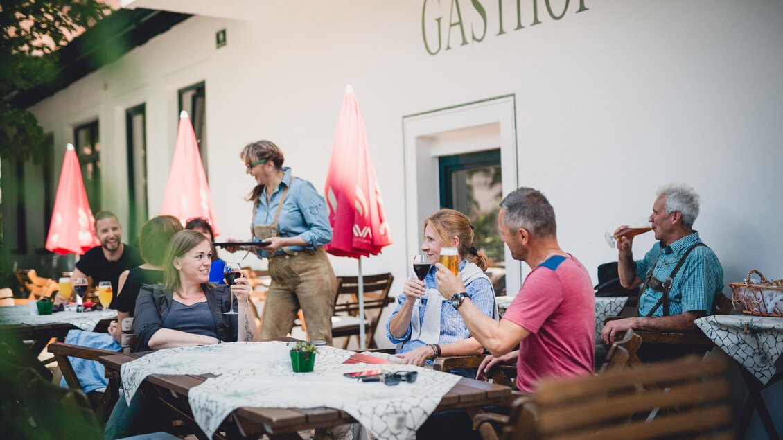 Eine gesellige Runde von Menschen sitzt im Freien vor einem Gasthof. Einige genießen Getränke, während eine Kellnerin einen Tisch bedient. | © GH Schäffer_Neuberg (C) Seiser_Karner