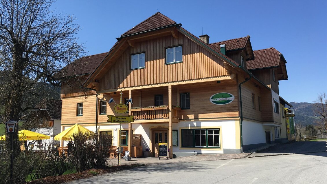 Ein gemütliches Holzhaus mit mehreren Stockwerken und einem einladenden Eingang. Vor dem Gebäude sind Tische im Freien aufgestellt, ideal für Gäste. | © Tourismusverband Murau