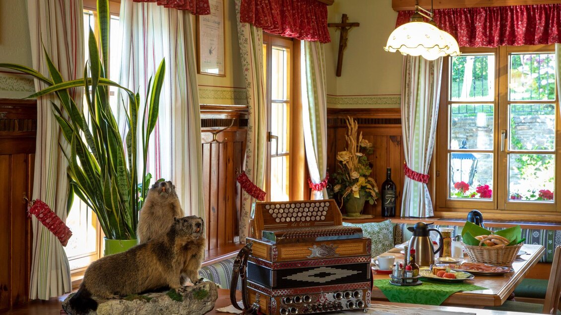 Ein gemütlicher Raum mit einem Holztisch und traditioneller Dekoration. Auf dem Tisch steht ein Akkordeon und zwei Murmeltiere sind als Dekoration platziert. | © TV Region Graz - Lunghammer