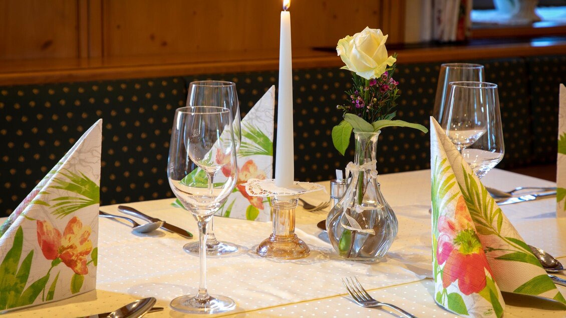 Ein elegant gedeckter Tisch mit Glaswaren, Servietten und einer einzelnen Rose in einer kleinen Vase. Auf dem Tisch brennt eine Kerze und die Dekoration hat einen floralen Touch. | © TV Region Graz - Lunghammer