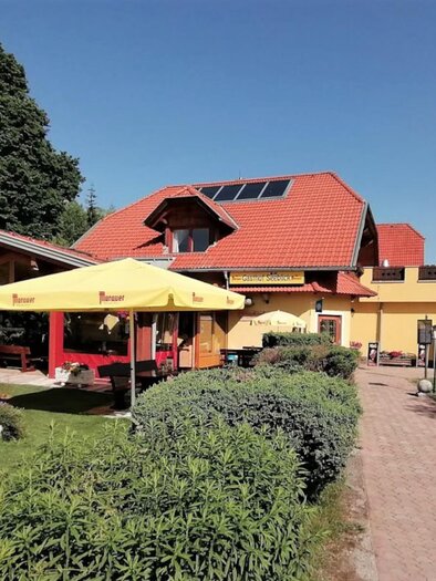 A restaurant with a yellow facade and a red roof. Outside, there are terraces with umbrellas and a green garden landscape. | © Gasthof Seeblick