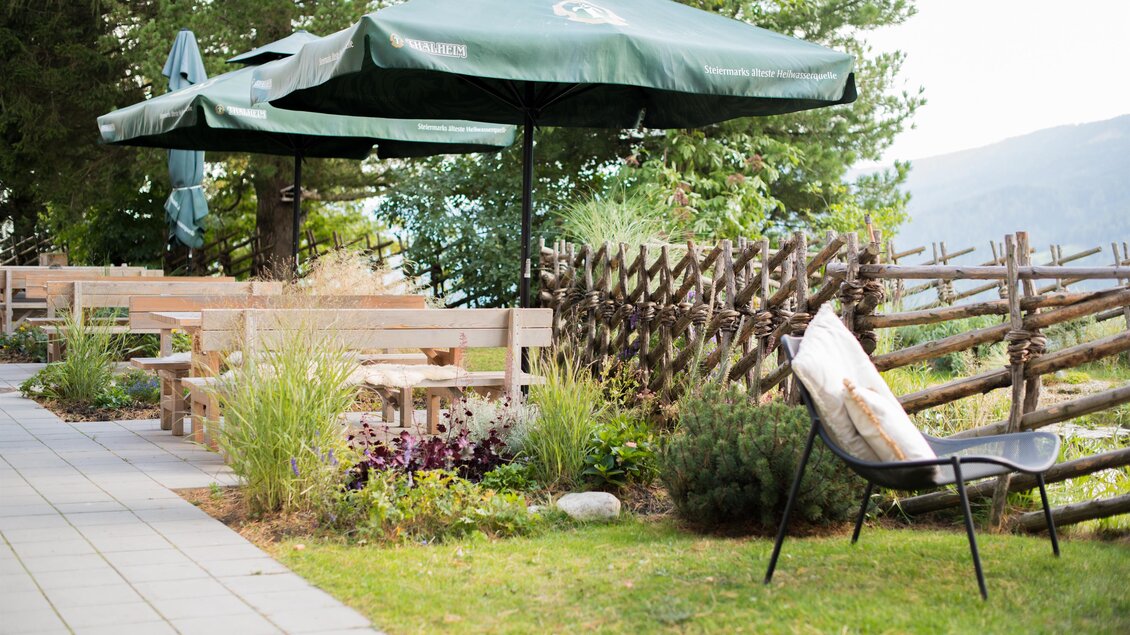 Ein gemütlicher Außenbereich mit Gartenmöbeln und Sonnenschirmen. Im Hintergrund ist eine natürliche Kulisse mit Bäumen und einem Zaun zu sehen. | © Erlebnisregion Murtal