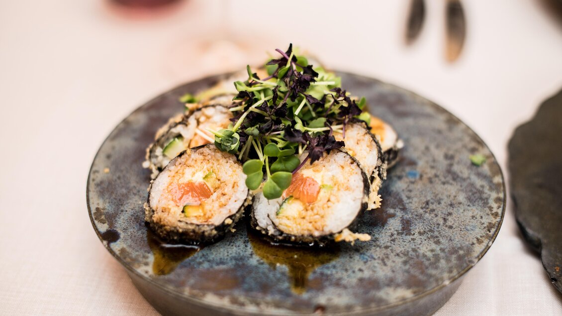 Ein Teller mit Sushi-Rollen, garniert mit frischen Kräutern. Das Gericht ist auf einem dekorativen, dunklen Teller angerichtet. | © Erlebnisregion Murtal