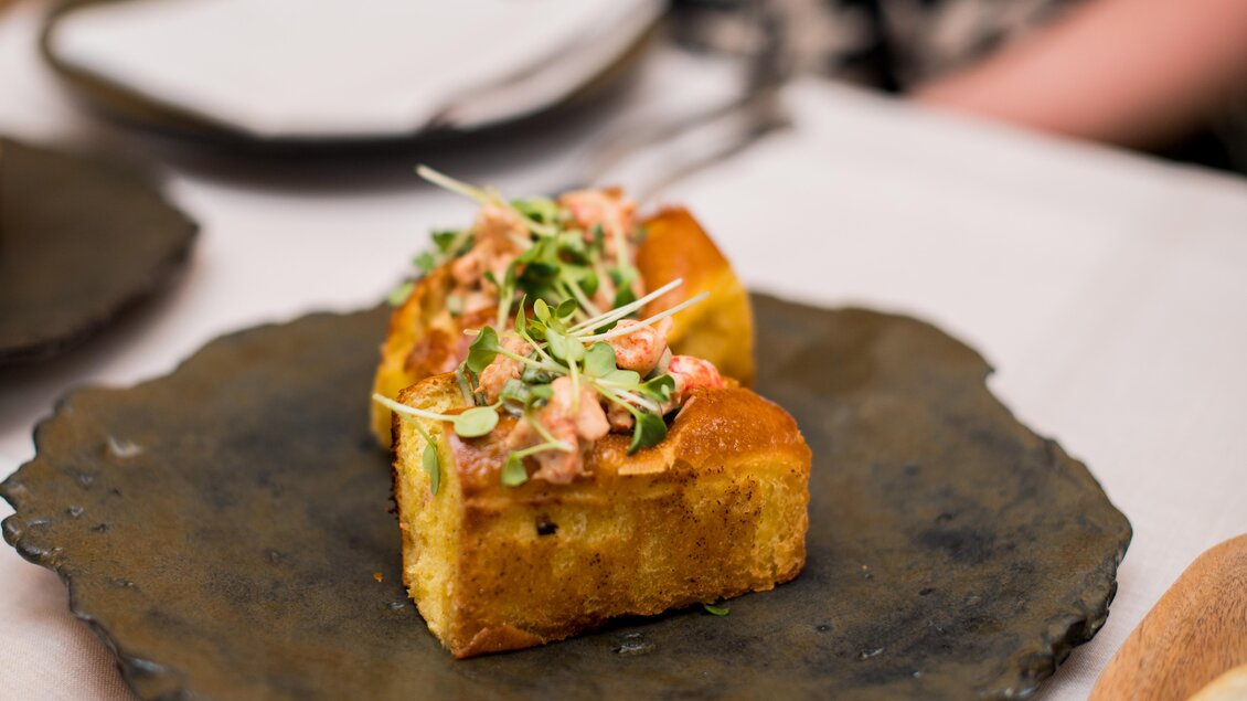 Ein köstlicher Teller mit zwei Stückchen Brot, belegt mit einer Mischung aus Lachs und frischen Kräutern. Die Speise ist auf einem rustikalen Teller angerichtet. | © Erlebnisregion Murtal
