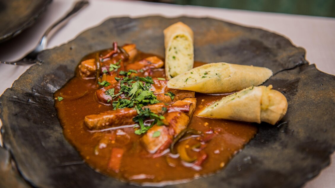 Ein leckeres Gericht mit Würstchen in einer würzigen Soße, garniert mit frischen Kräutern. Daneben liegen mehrere Stücke knuspriges Brot. | © Erlebnisregion Murtal