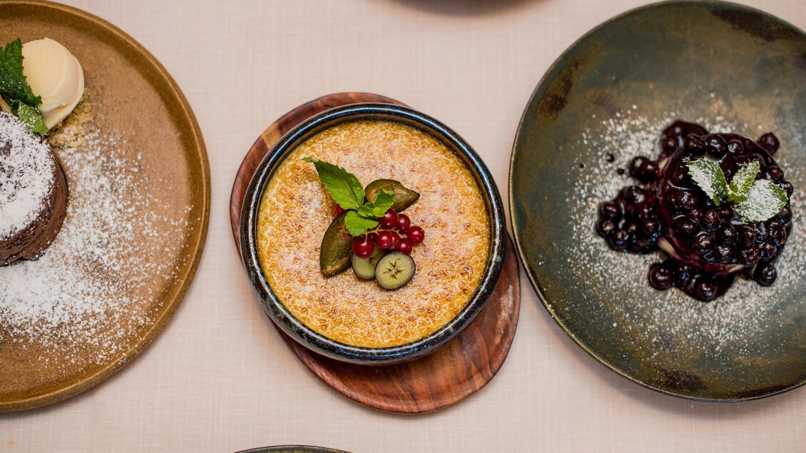 Ein elegantes Dessert in einem runden Schüsselchen, garniert mit frischen Beeren und Minze. Daneben befinden sich zwei weitere Teller mit verschiedenen Leckereien. | © Erlebnisregion Murtal