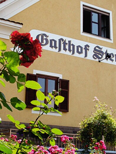 A traditional inn with the sign "Gasthof Sternwirt". Colorful flowers frame the facade of the house. | © Sternwirt