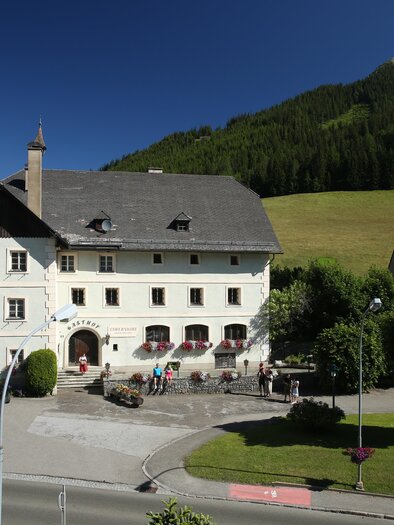 Ein malerisches Gebäude in einer ländlichen Umgebung, umgeben von Bäumen und einer sanften Hügelkette. Es ist ein sonniger Tag mit klarem Himmel. | © Erlebnisregion Murtal