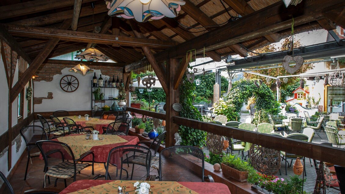 Ein gemütlicher Restaurantbereich mit Holzdecke und Tischen, die eingedeckt sind. Im Hintergrund sind weitere Sitzgelegenheiten im Freien und viel Grün zu sehen. | © TV Region Graz - Lunghammer