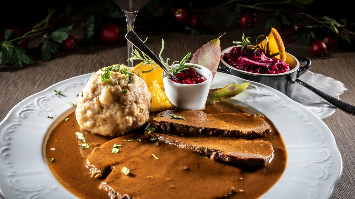 Ein Teller mit zartem Fleisch in einer schmackhaften Soße, serviert mit Knödeln und einer Beilage aus Rotkraut. Dazu gibt es fruchtige Garnitur und Saucen. | © TV Region Graz - Lunghammer