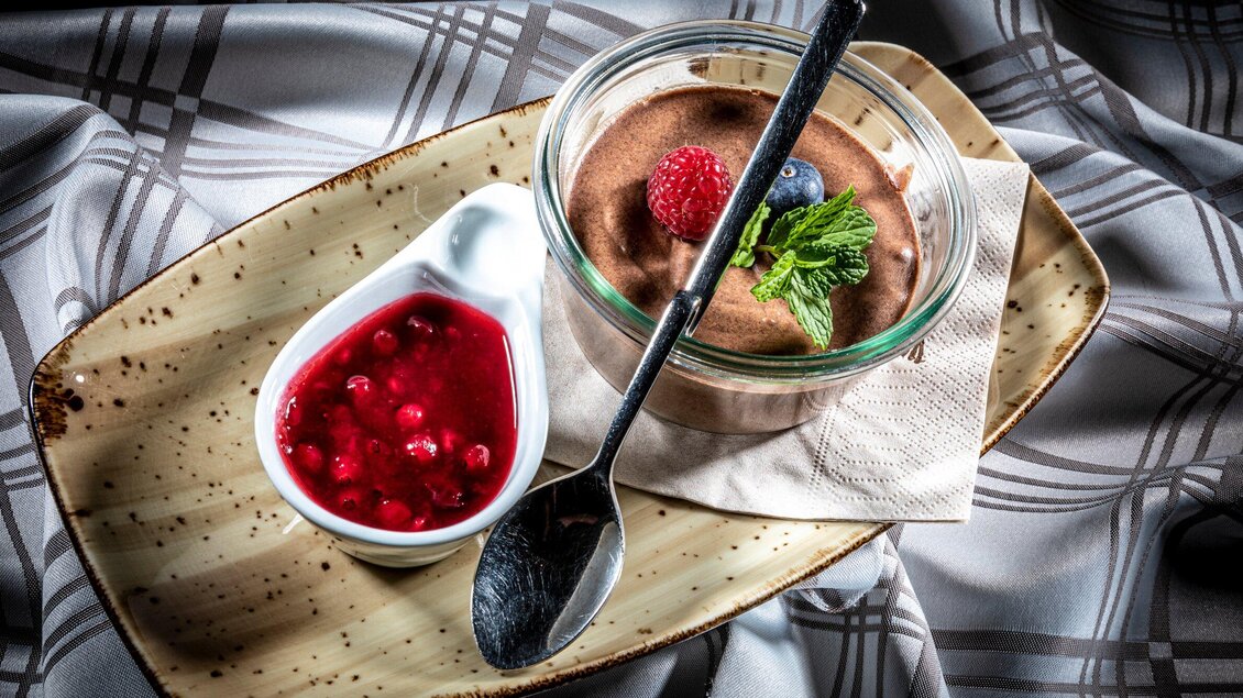 Ein köstliches Schokoladenmousse in einem Glas, garniert mit einer Himbeere und einer Blau- oder Erdbeere. Daneben befindet sich eine Schale mit roter Fruchtsoße. | © TV Region Graz - Lunghammer