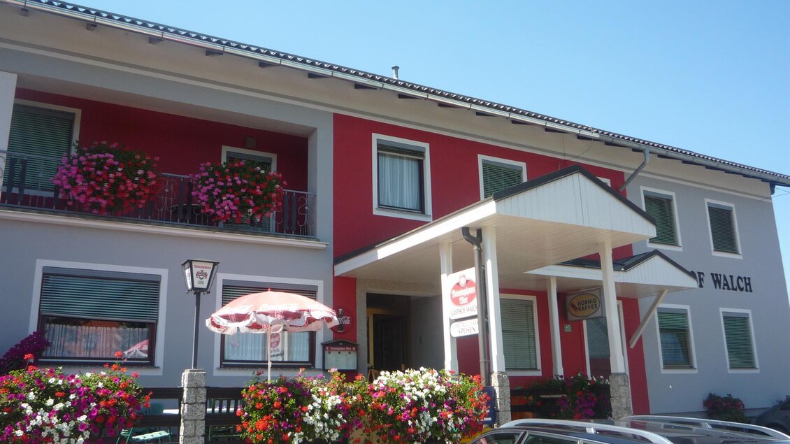 Ein charmantes Gebäude mit bunten Blumen und einem einladenden Eingangsbereich. Die Fassade ist in leuchtenden Farben gestaltet, was eine freundliche Atmosphäre schafft. | © Gasthaus Walch