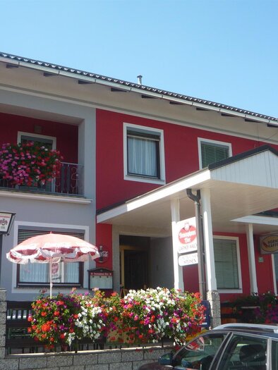 Ein charmantes Gebäude mit bunten Blumen und einem einladenden Eingangsbereich. Die Fassade ist in leuchtenden Farben gestaltet, was eine freundliche Atmosphäre schafft. | © Gasthaus Walch