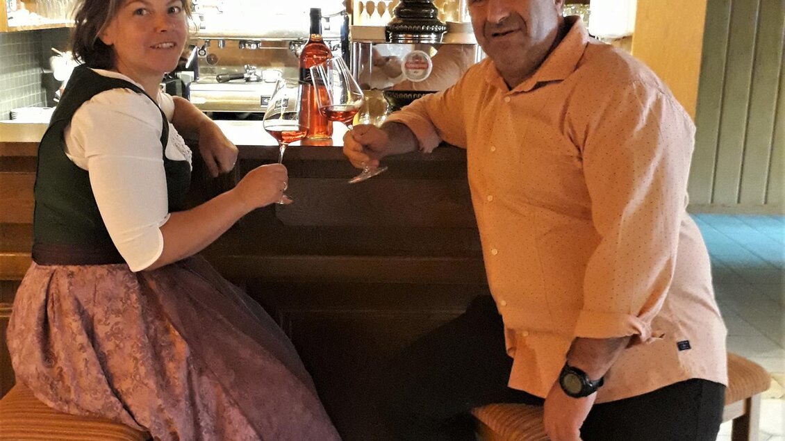 Eine Frau und ein Mann sitzen an einer Bar. Im Hintergrund sind zahlreiche Flaschen und ein warmes Ambiente zu sehen. | © TV Lipizzanerheimat