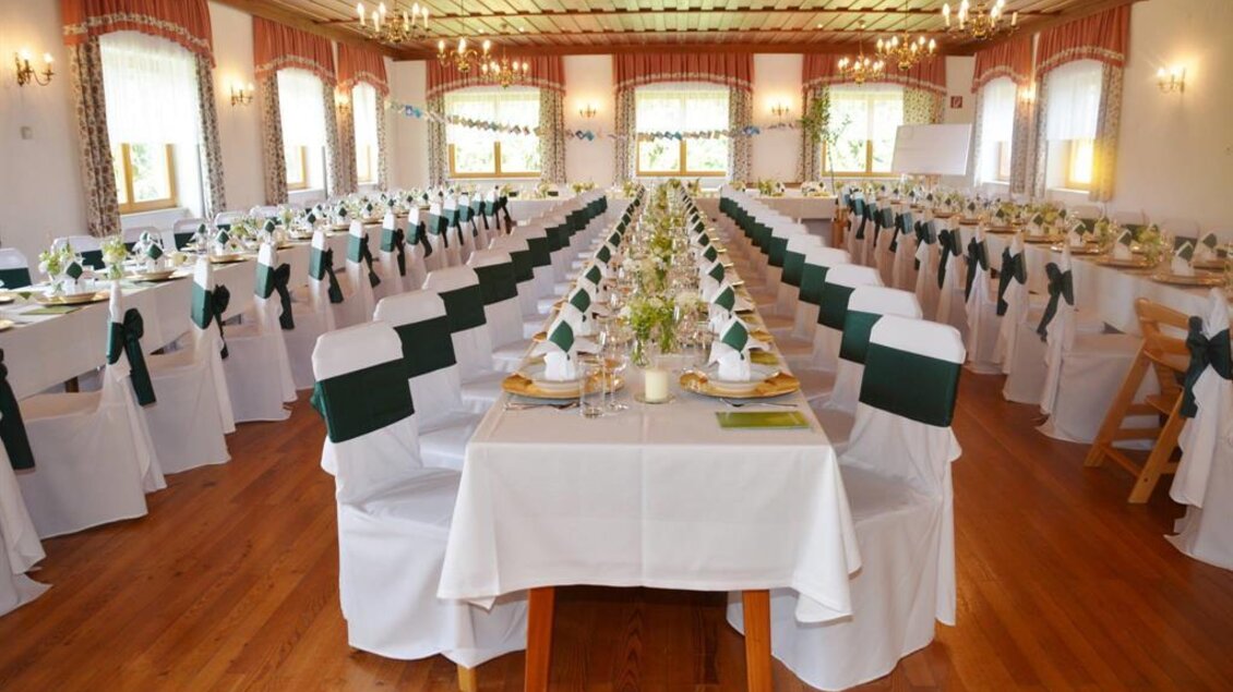 Ein eleganter Festsaal mit gedeckten Tischen und Stühlen. Die Tische sind hübsch dekoriert und mit weißen Tischdecken und grünen Schleifen geschmückt. | © Gasthof Wiendl