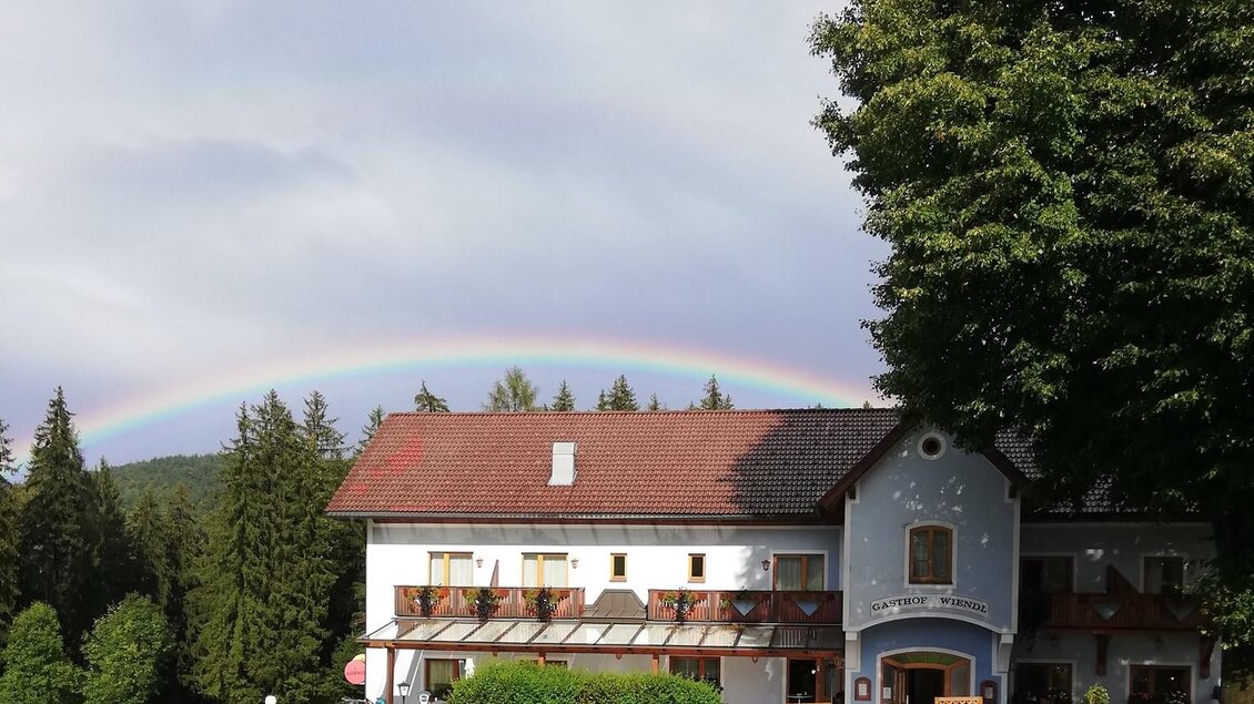 Ein schönes Haus in der Natur mit einem Regenbogen im Hintergrund. Umgeben von Bäumen und einem klaren Himmel. | © Keine Kenntnis