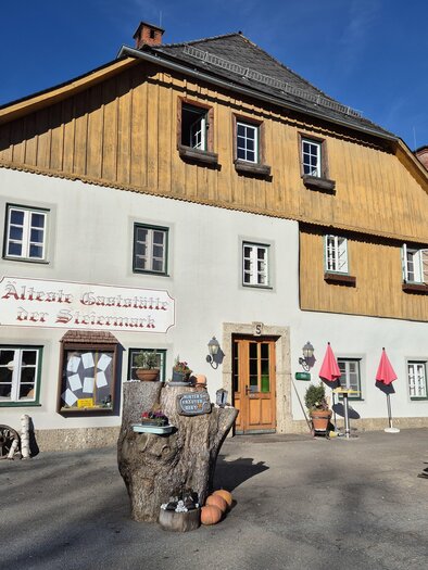 A charming inn with a wooden facade and classic windows. In front of the building, there are flowers and a large wooden table. | © Tourismusverband Murau