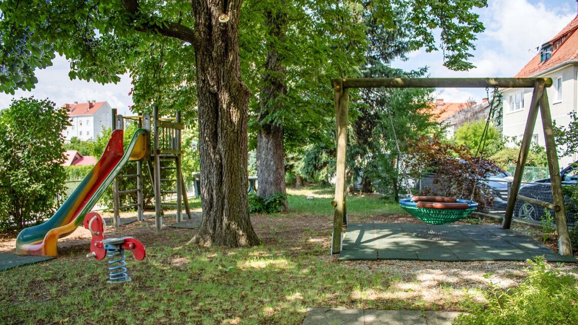 Ein Spielplatz mit einer Rutsche, einer Schaukel und einem Wippen. Umgeben von Bäumen und Büschen in einer ruhigen Umgebung. | © Gasthof s'Reindl