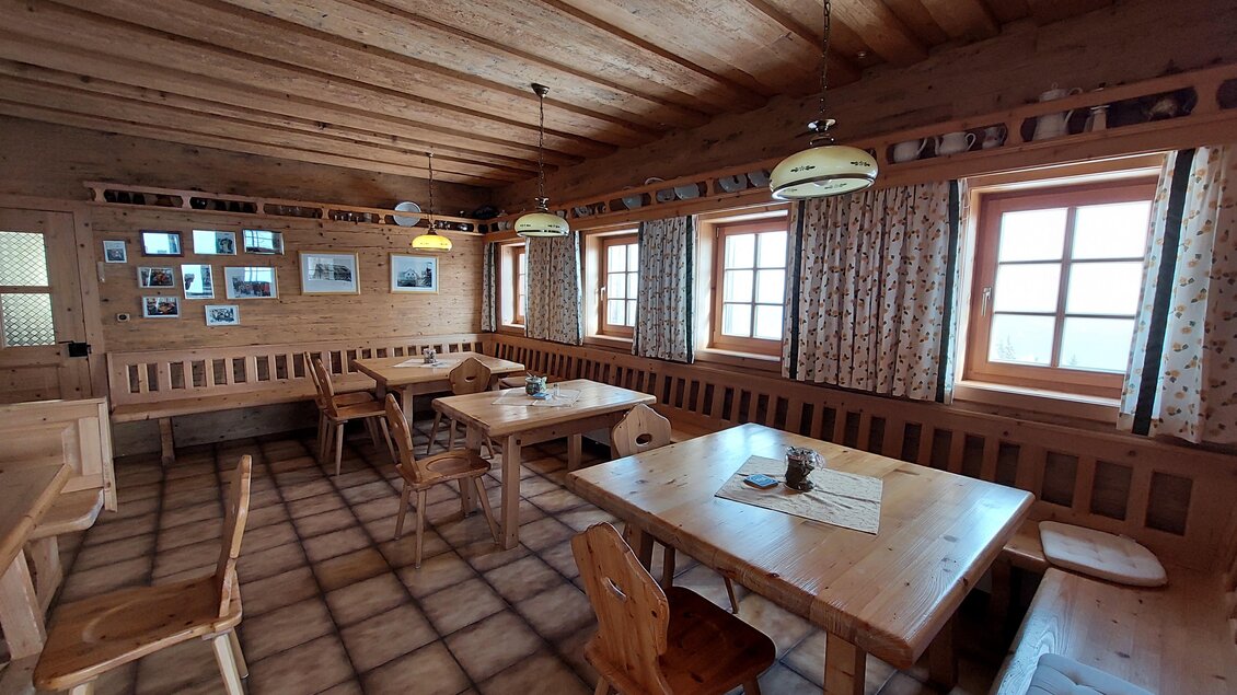 Ein gemütlicher Innenraum mit Holzmöbeln und Fenstern, die viel Licht hereinlassen. An den Wänden hängen Fotos, die eine einladende Atmosphäre schaffen. | © TV Hochsteiermark / Brigitte Digruber